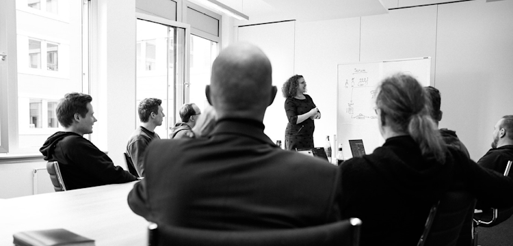 Mehrere Personen sitzen entspannt in einem Besprechungsraum an einem Tisch mit Laptops und Getränken. Sie unterhalten sich und lachen, die Szene wirkt locker und kollegial. Das Schwarz-Weiß-Foto zeigt die Gruppe aus einer seitlichen Perspektive.